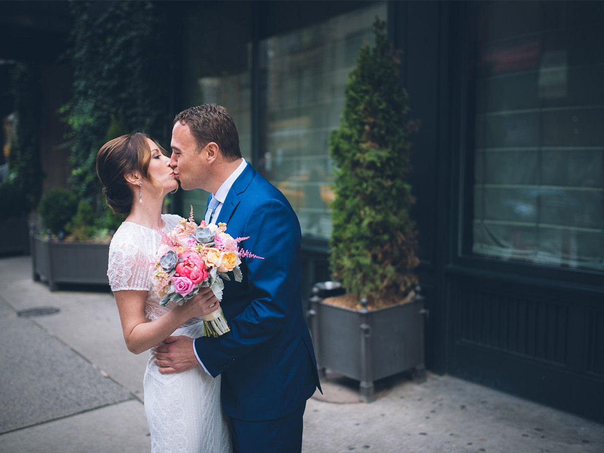 Newly wed couple kiss with flowers in hand
